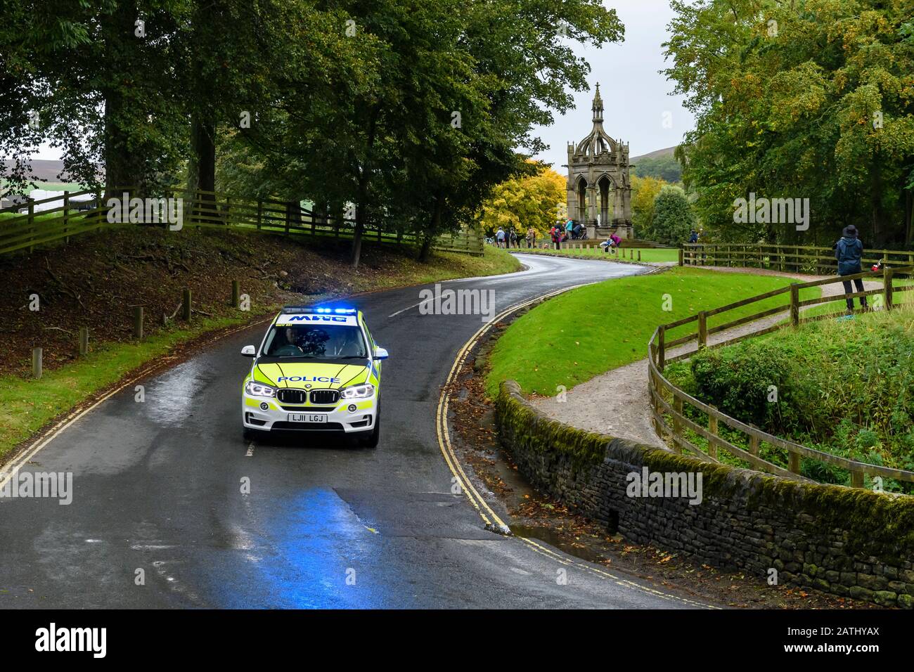 Auto della polizia che guida e viaggia sulla corsia di campagna con luci blu lampeggianti (veicolo di controllo del traffico BMW all'evento) - Bolton Abbey, Yorkshire, Inghilterra UK Foto Stock