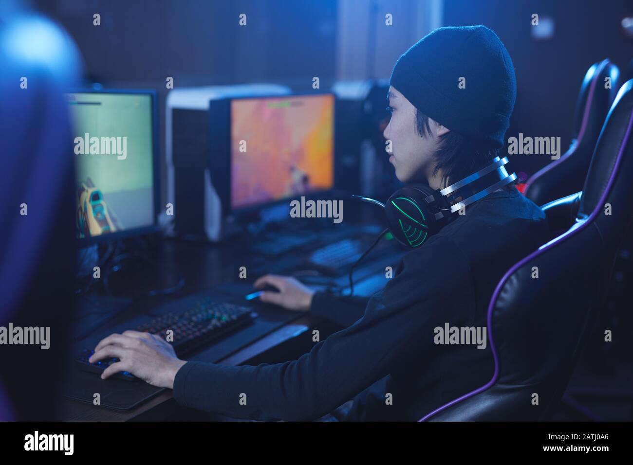 Ritratto della vista posteriore di pro-gamer asiatici che giocano a videogame mentre si siedono nel cyber interiore scuro, copia spazio Foto Stock