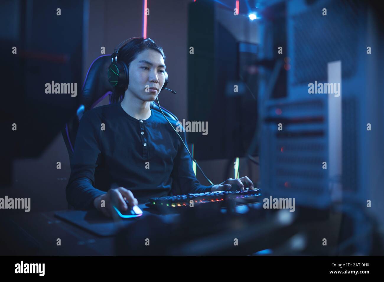 Ritratto di giovane asiatico che usa il computer in scuro cyber interno, copia spazio Foto Stock
