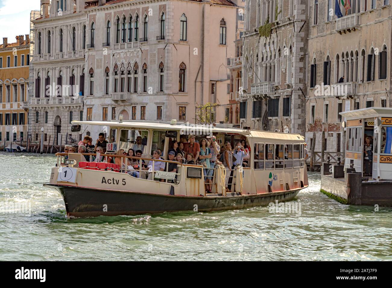 I passeggeri a bordo di un vaporetto o vaporetto n. 1 che parte dalla fermata del vaporetto Ca' Rezzonico lungo il Canal Grande a Venezia Foto Stock