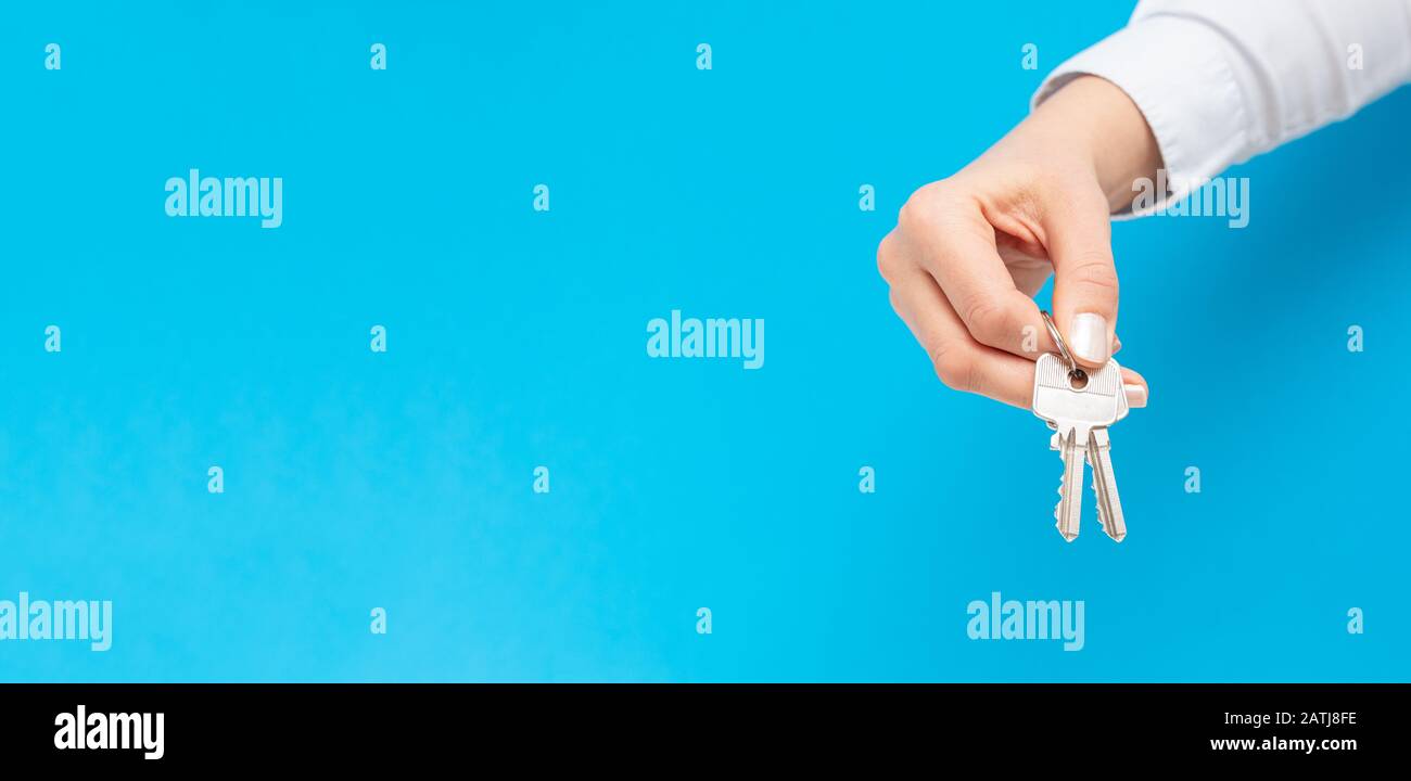 Mano femminile che tiene e che dà la chiave della casa sullo sfondo dello spazio della copia. Agente immobiliare. Foto Stock