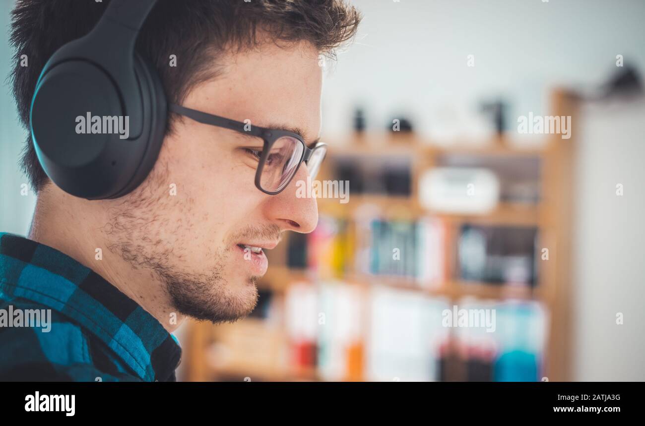 Giovane caucasico con camicia blu controllata sta elencando alla musica con le cuffie senza fili Foto Stock