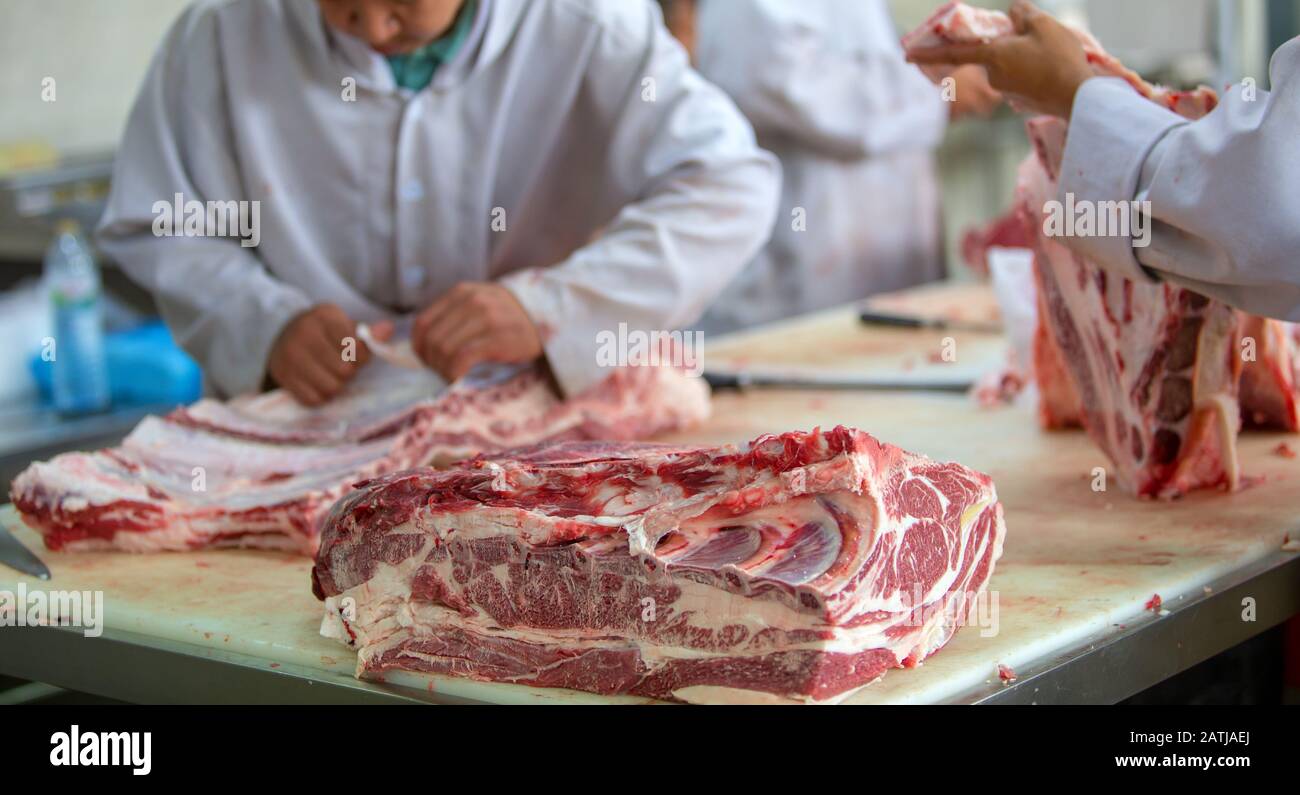Il macellaio che taglia la carne cruda nel macelleria Foto Stock