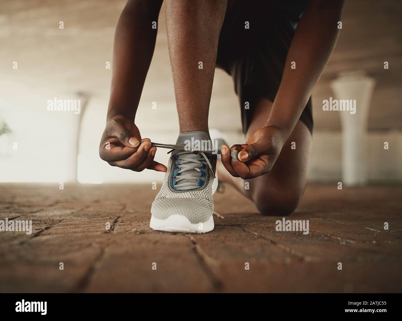 Immagine ritagliata delle mani che legano le scarpe della sneaker sulla superficie del pavimento Foto Stock