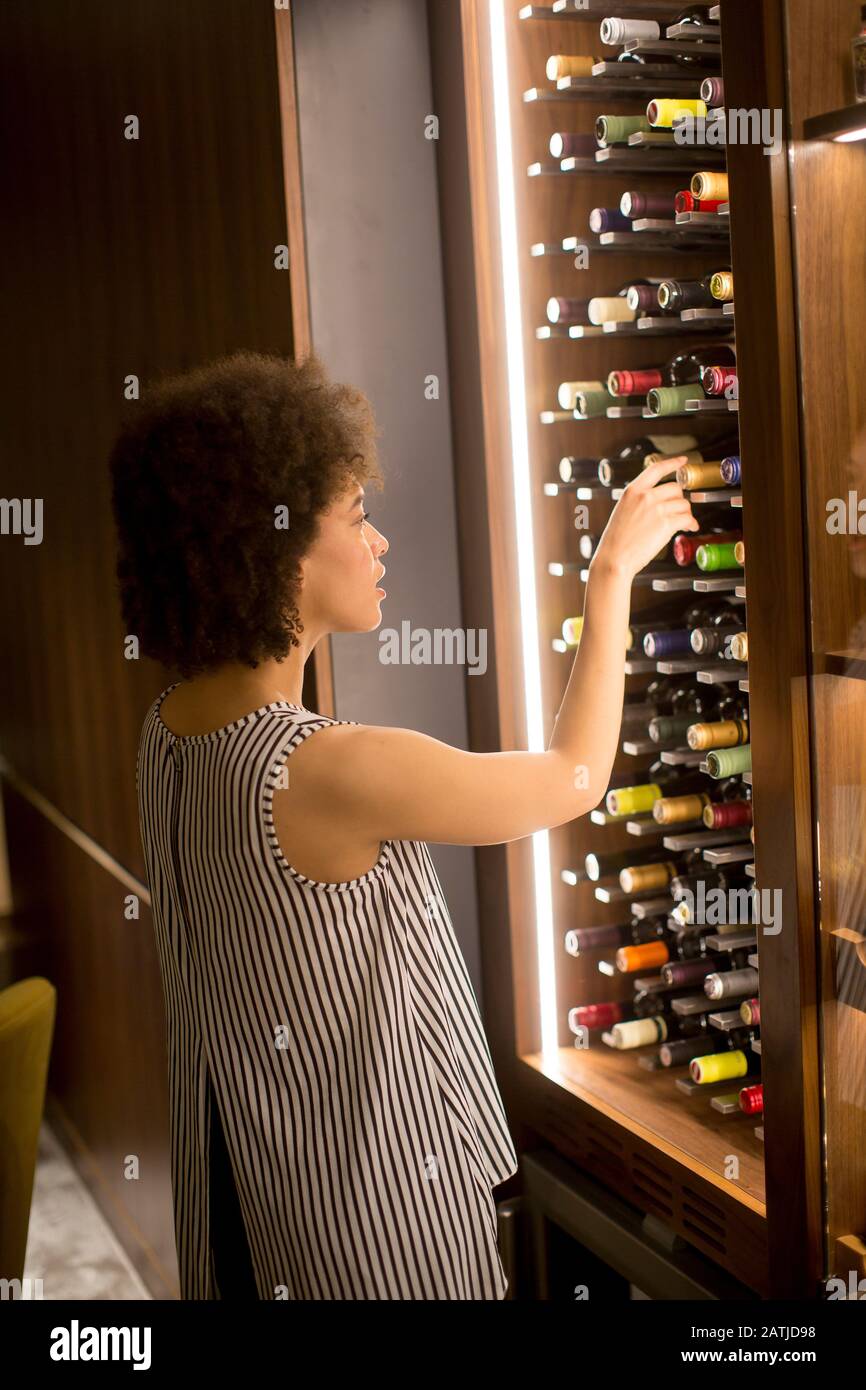Giovane donna afroamericana che sceglie una bottiglia di vino rosso Foto Stock