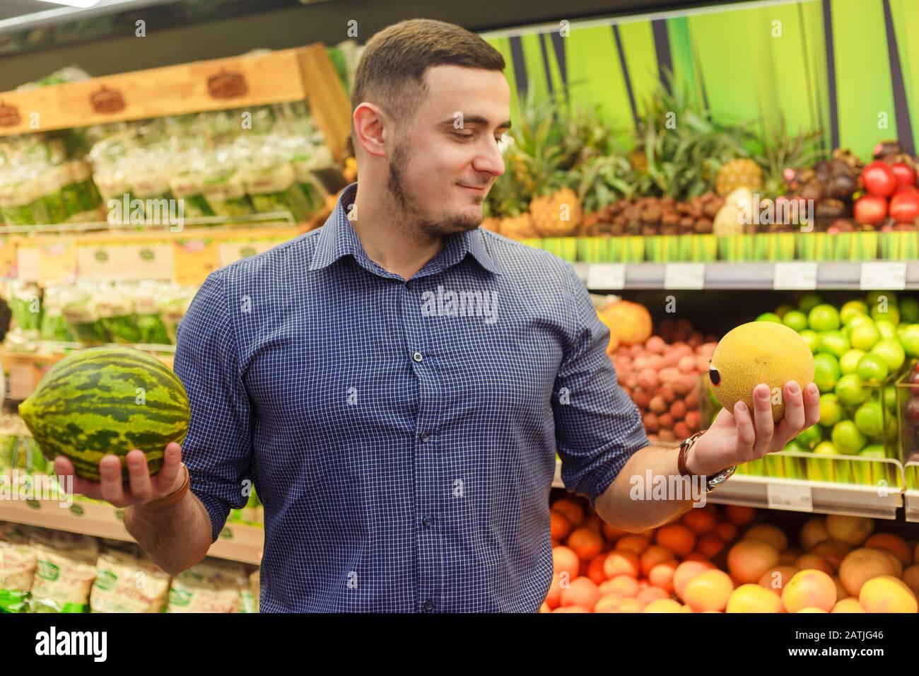 Giovane uomo in negozio di alimentari presso il reparto frutta sceglie tra melone e anguria. Foto Stock