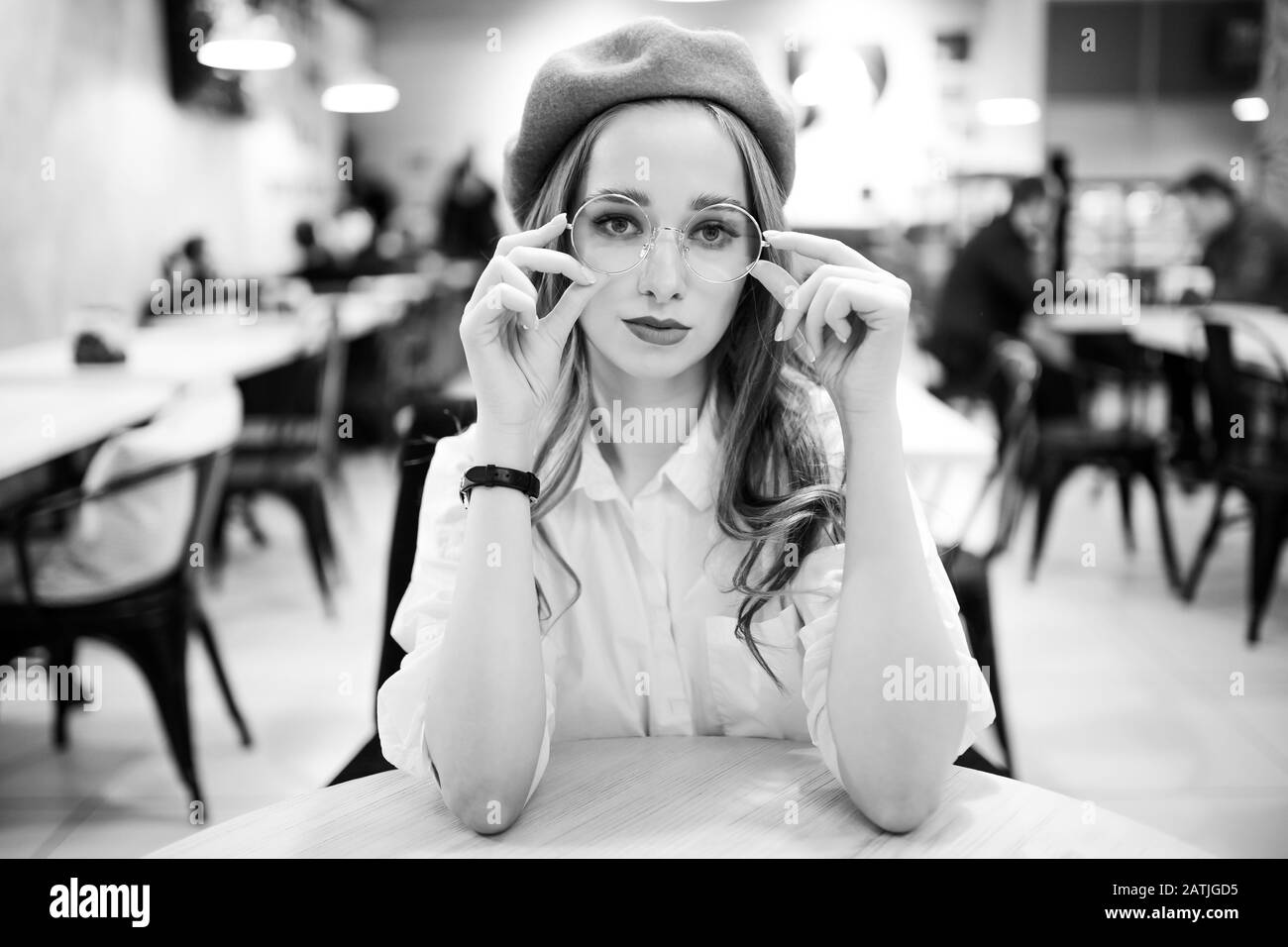 Ritratto bianco-nero di giovane donna con occhiali e beretto in caffè, guardando in cornice, concentrato Foto Stock
