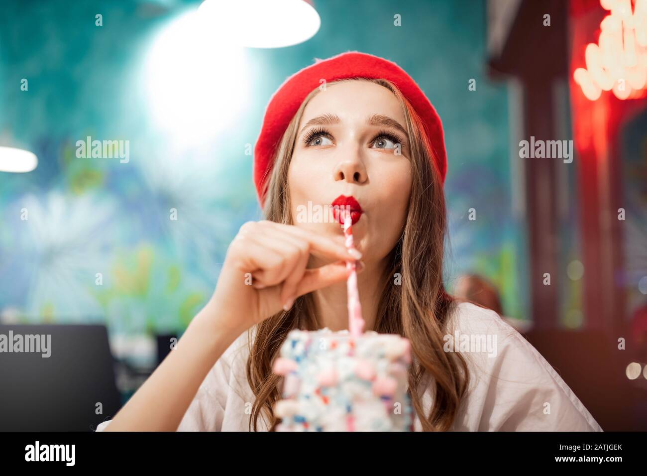 Ragazza con denti bianchi, bel sorriso in berretto rosso, Francia bevande rosa fragola milkshake dalla paglia Foto Stock