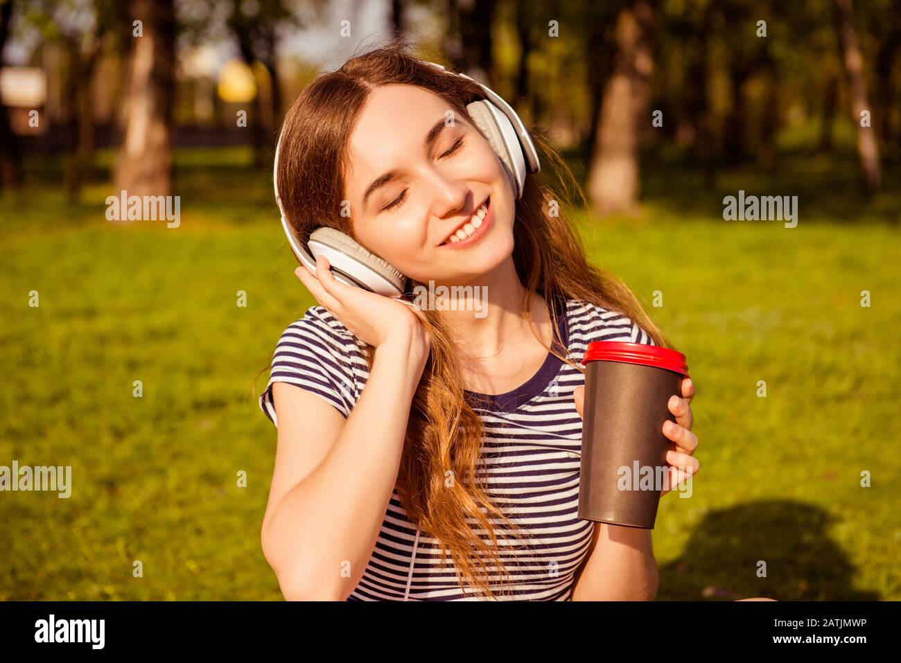 Ritratto di felice rilassato donna ascoltare musica in cuffie e bere caffè Foto Stock