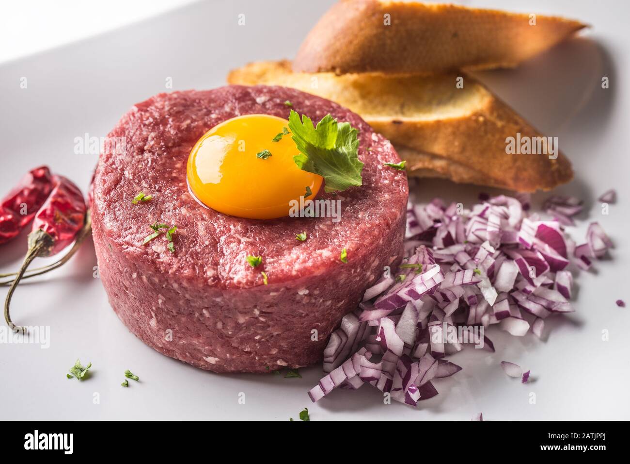 Tartare di manzo con tuorlo d'uovo cipolla rossa peperoncino peperoni erbe e bruschetta Foto Stock