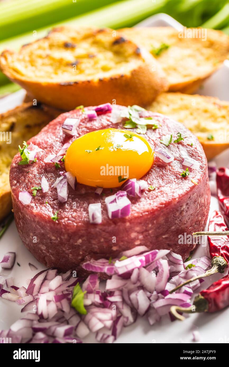 Tartare di manzo con tuorlo d'uovo cipolla rossa peperoncino peperoni erbe e bruschetta Foto Stock