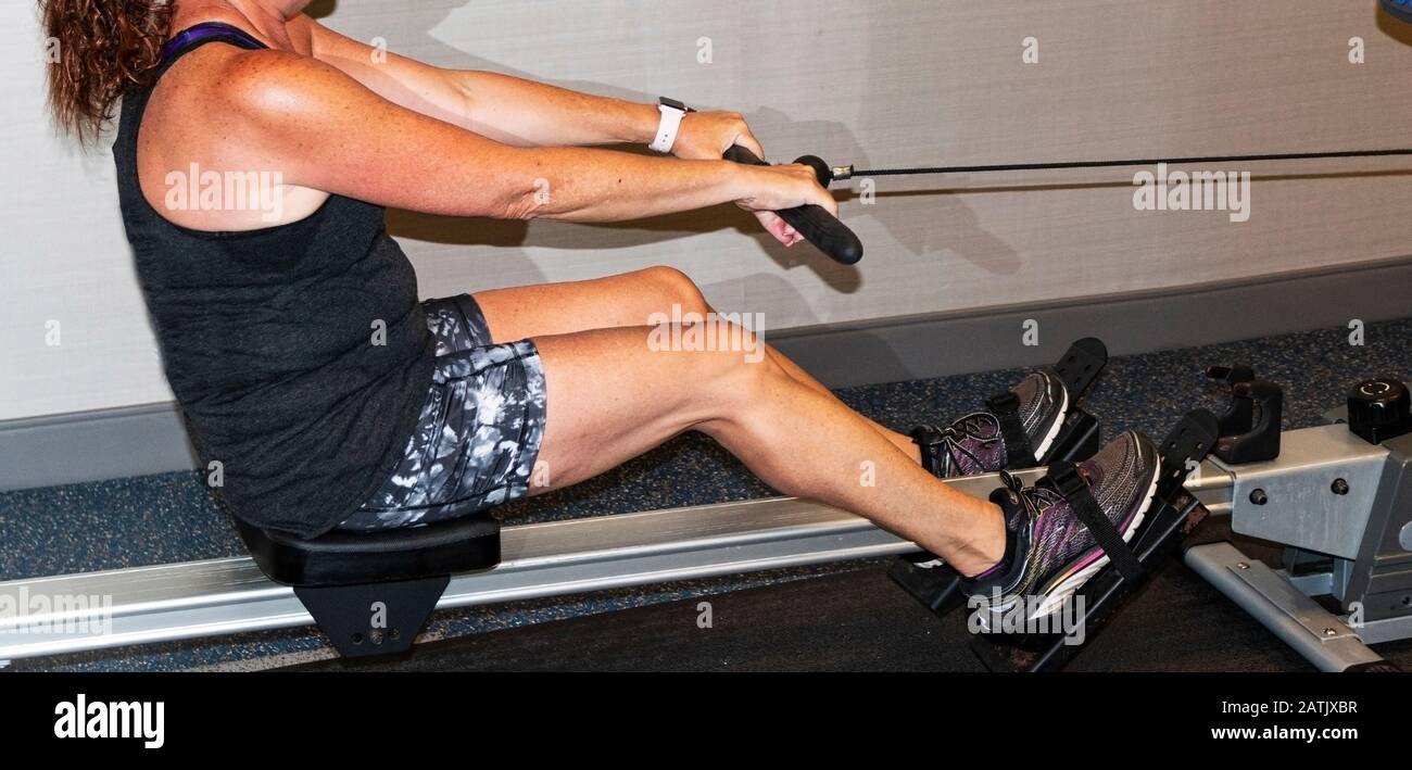 Una donna caucasica sta tirando la corda mentre sta lavorando su una macchina a remi all'interno in una palestra. Foto Stock