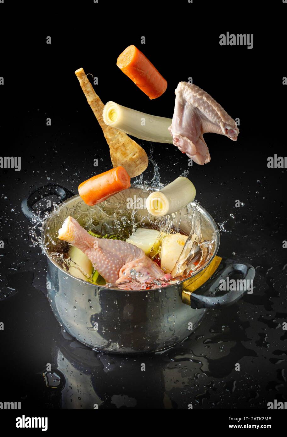Ingredienti per fare il brodo volare verso un piatto con acqua spruzzata su sfondo nero Foto Stock