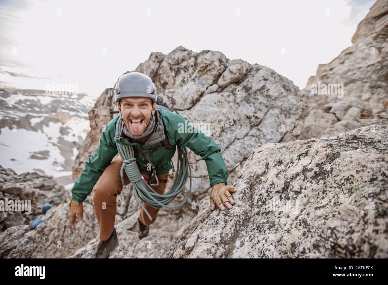 Scalatore di roccia maschio con corda e casco si stacca lingua fuori Foto Stock