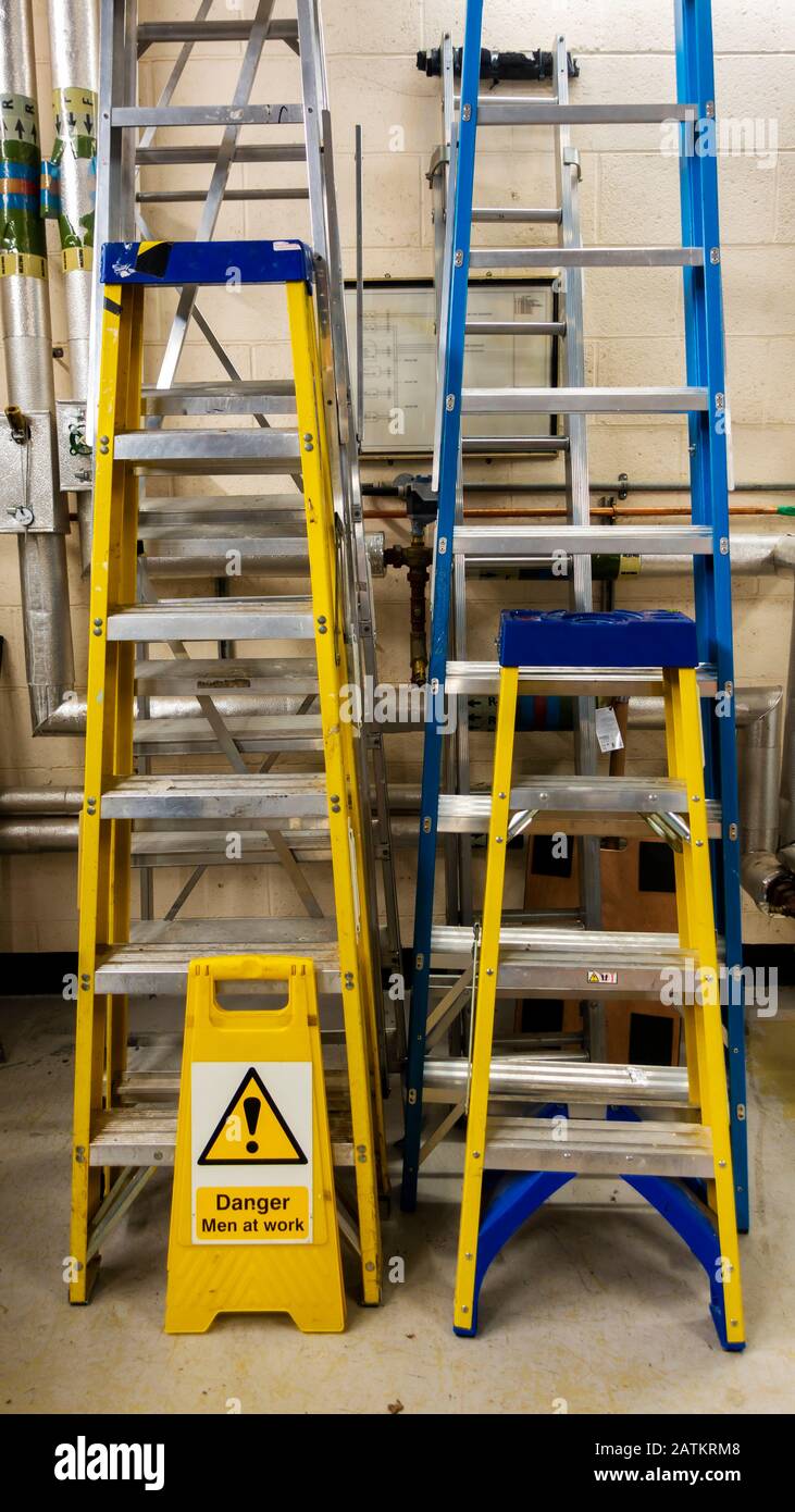 Vari set di scale e gradini in un laboratorio di manutenzione con un uomo in cantiere Foto Stock
