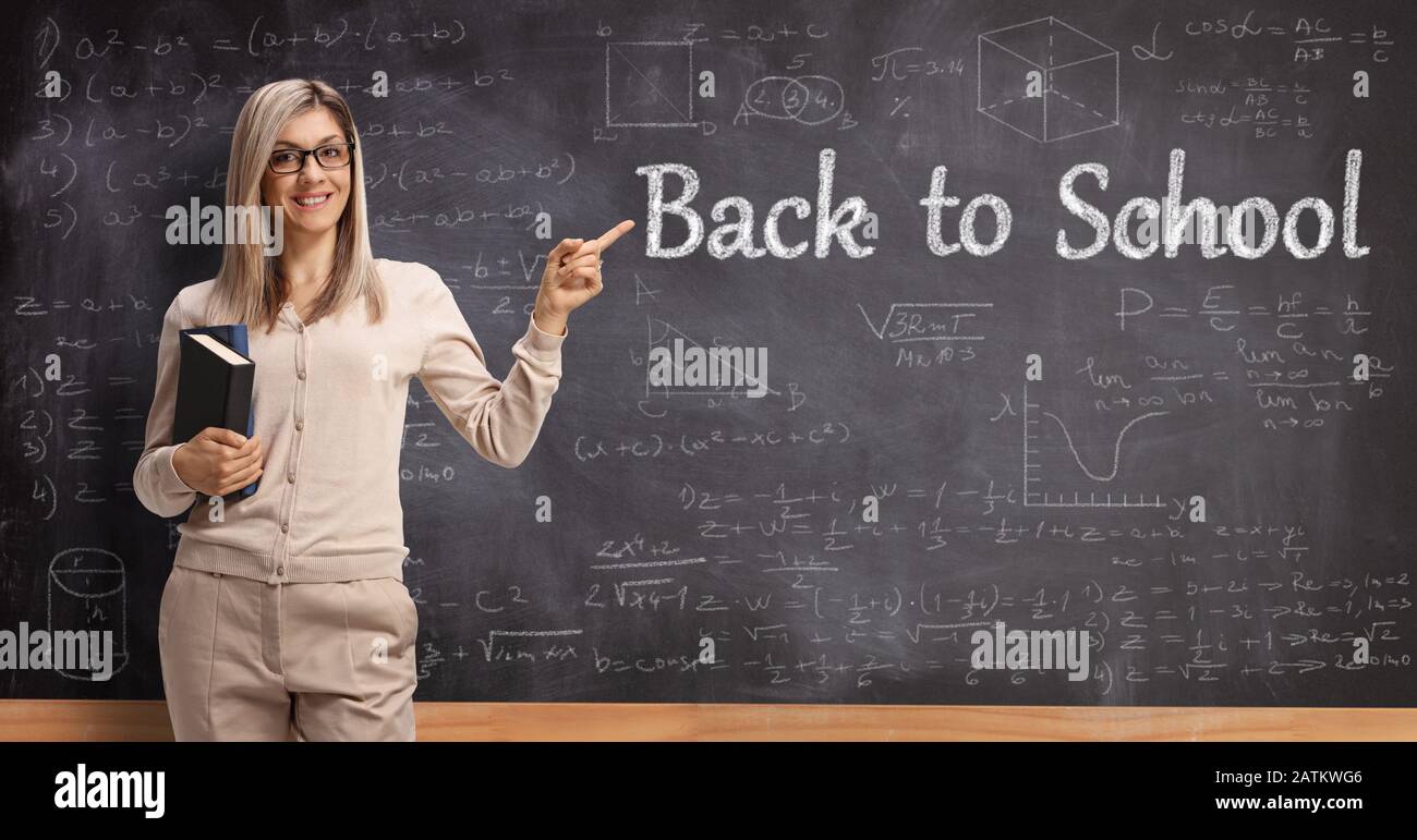 Giovane insegnante di sesso femminile che punta al testo di ritorno a scuola scritto su una lavagna Foto Stock
