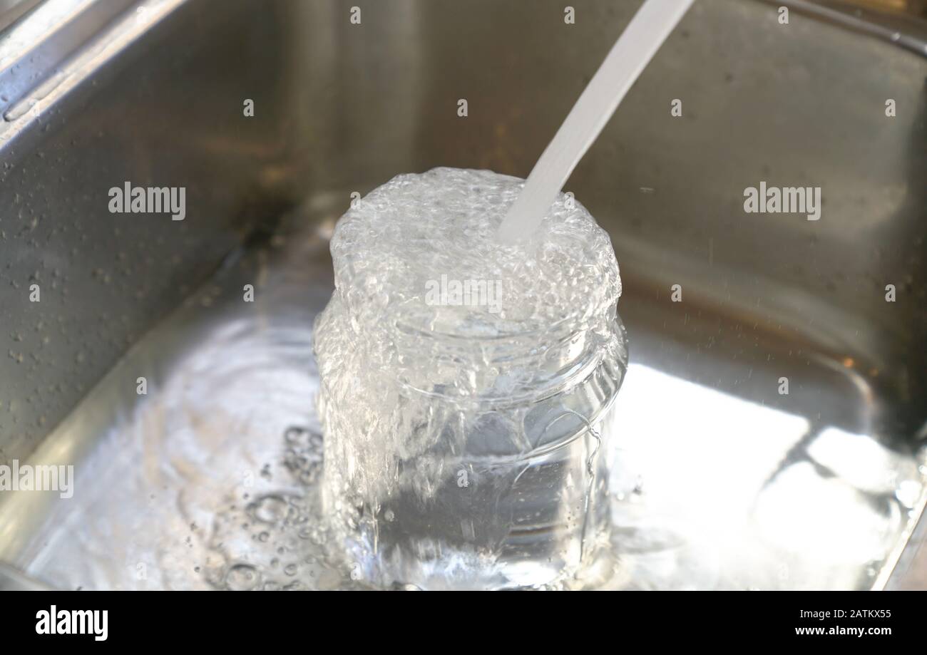 L'acqua dal rubinetto nel contenitore di plastica e trabocca al dispersore. Salva concetto di acqua. Foto Stock