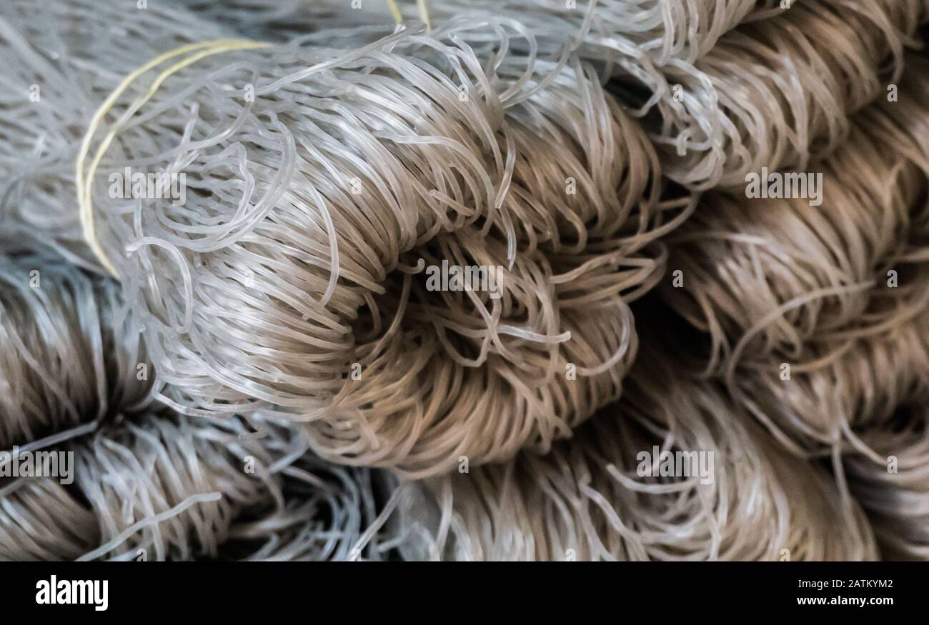 Tagliatelle di riso crude. Sono grigi e secchi, freschi e sani. Nel mercato assomiglia a threads.They sono su un'esposizione per la vendita. Fatto a mano. Foto Stock