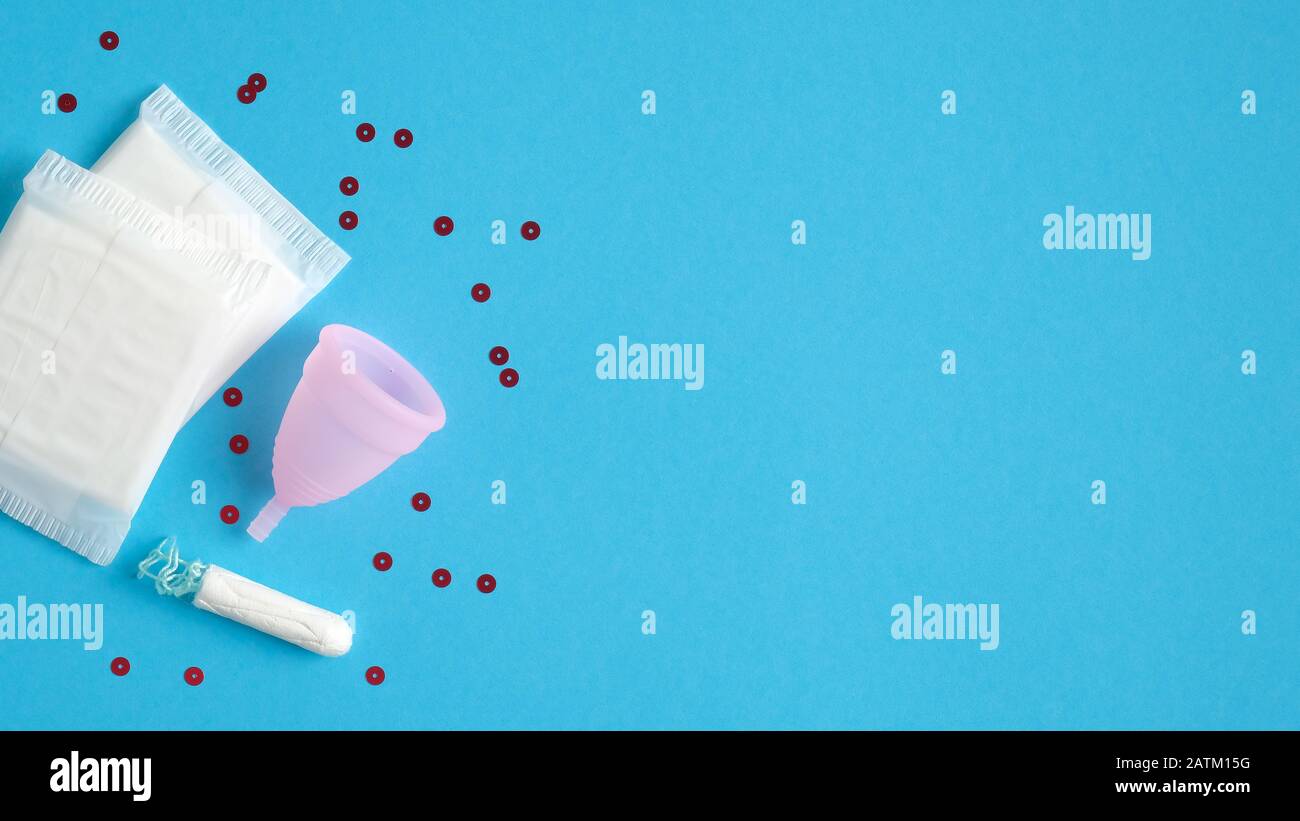 Set di prodotti per l'igiene femminile. Vista dall'alto sanitario pad, tampone, coppa mestruale su sfondo blu con confetti. Giorni critici, ciclo mestruale, fe Foto Stock