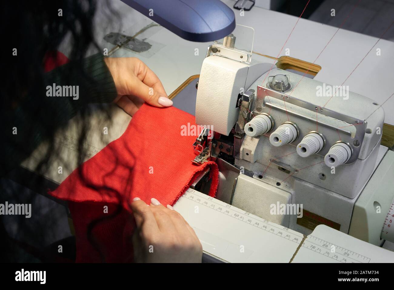 Giovane donna che usa una macchina da cucire da overlock professionale in officina. Attrezzatura per bordare, bordare o cucire abiti presso il negozio di sarti Foto Stock