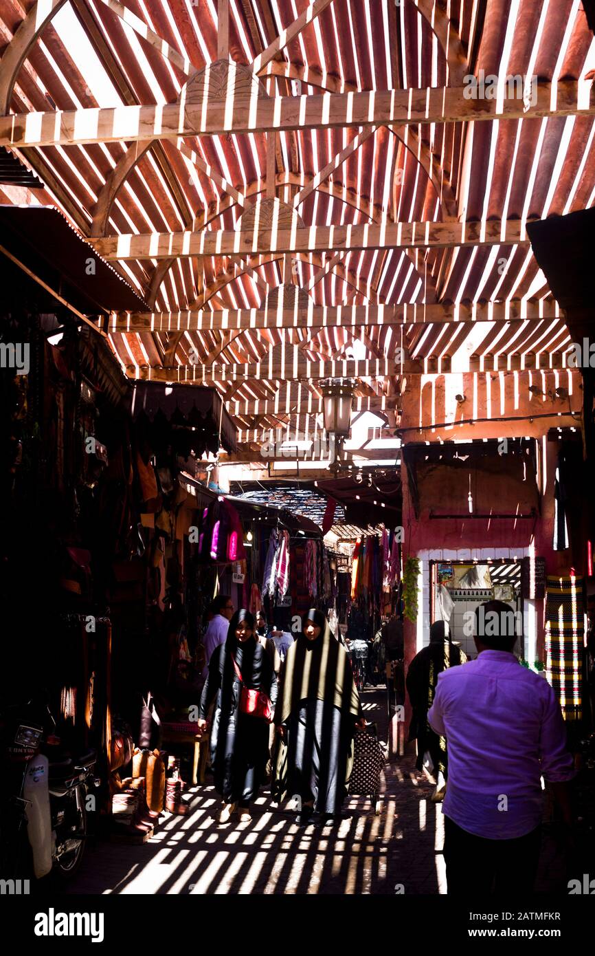 La luce del sole cade sugli acquirenti attraverso un tetto di doghe di legno in un mercato medina a Marrakech, Marocco Foto Stock