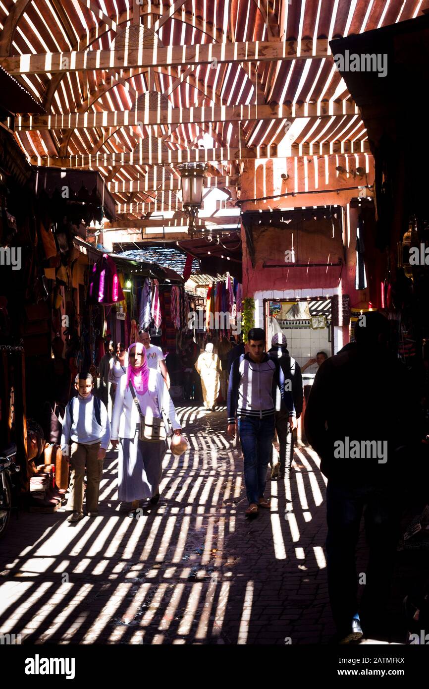 La luce del sole cade sugli acquirenti attraverso un tetto di doghe di legno in un mercato medina a Marrakech, Marocco Foto Stock