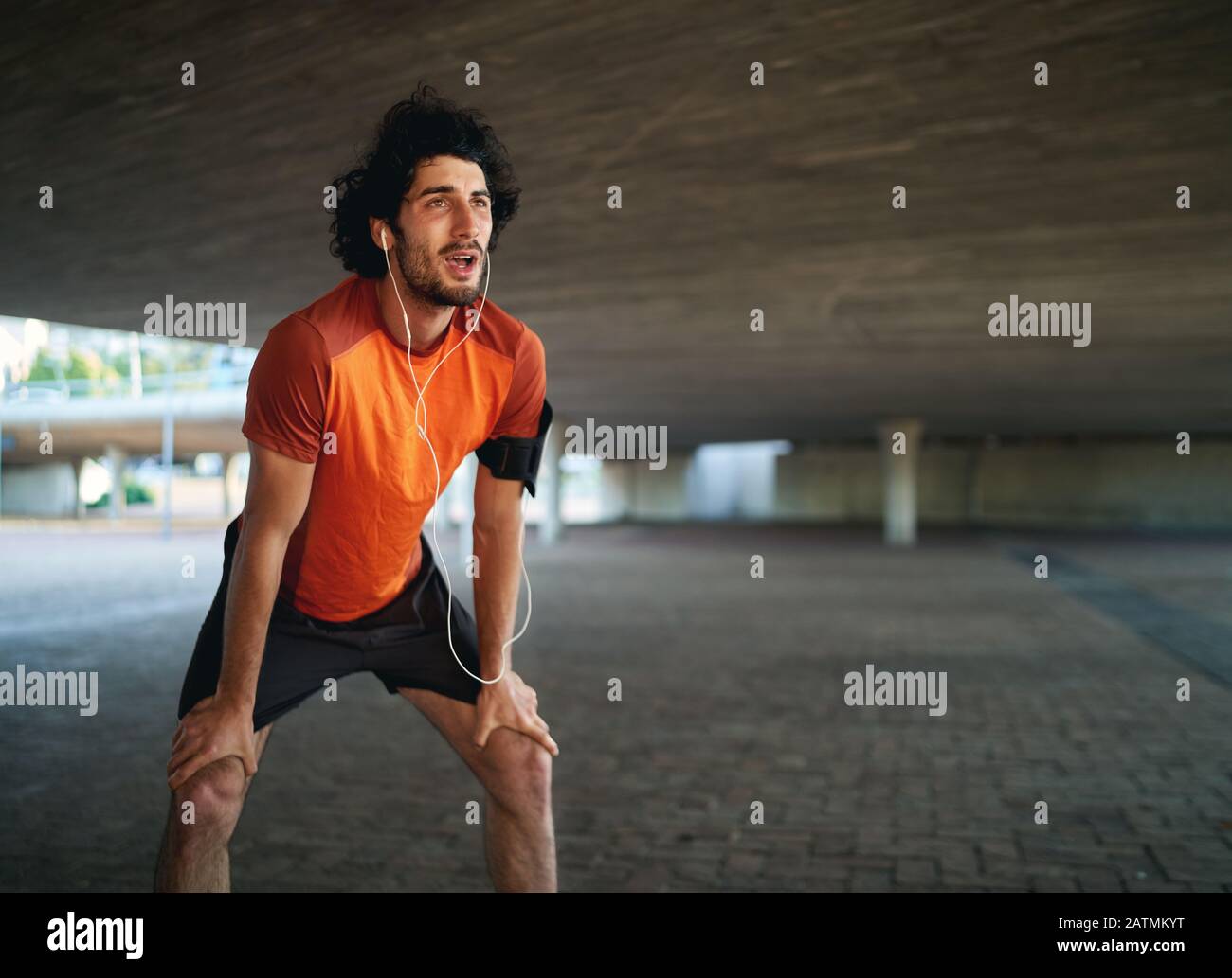 Ritratto di un atleta caucasico stanco uomo che ascolta la musica che prende respirare dopo un lungo periodo sotto il ponte Foto Stock