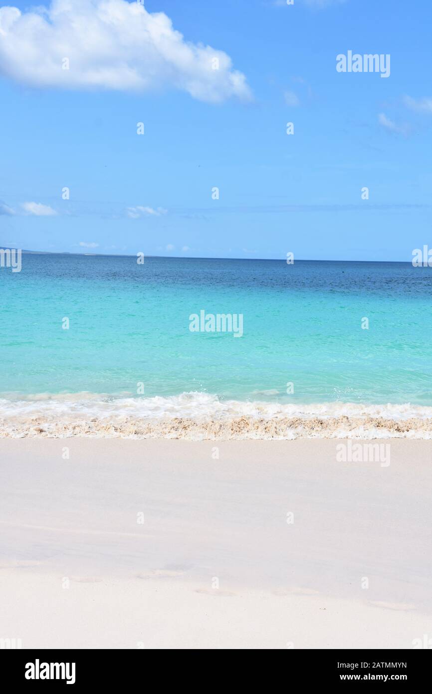 Spiaggia di sabbia tropicale e blu turchese oceano acqua sotto cielo blu Foto Stock
