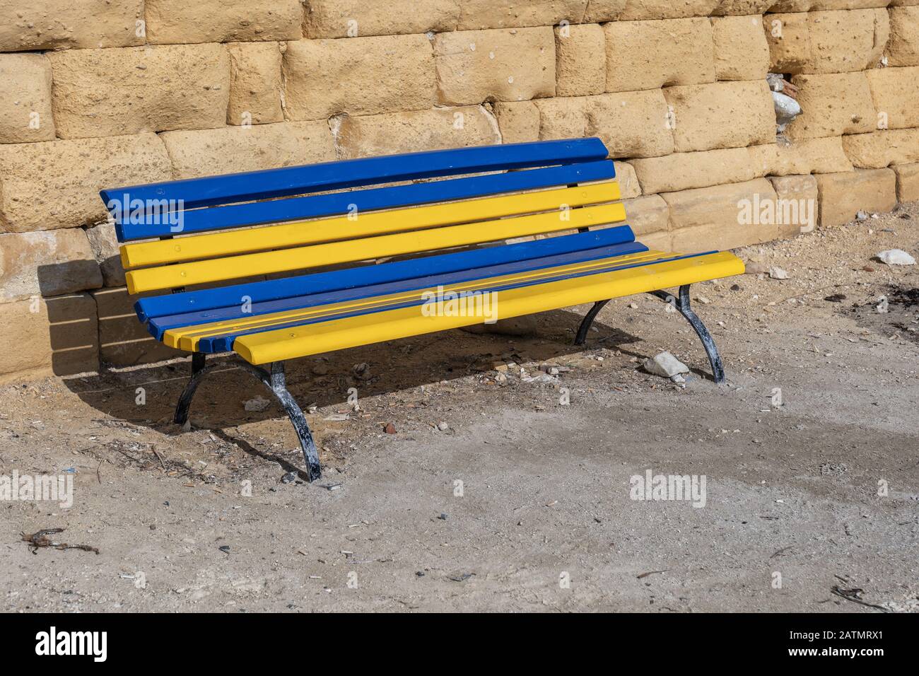 Panca in legno blu e giallo con supporto in metallo nella cittadina balneare di Marsaxlokk, Malta Foto Stock