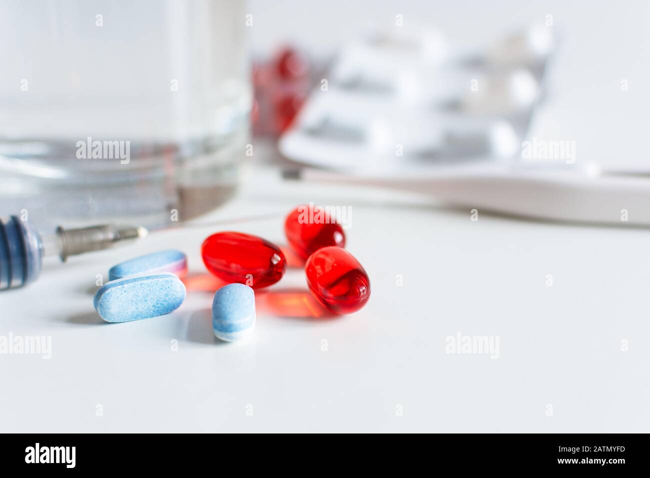 Pillole rosse e blu con termometro e si suringe su sfondo bianco. . Concetto di focolaio di virus. Trattamento freddo e influenzale. Coronavirus 2019-nCoV. Foto Stock