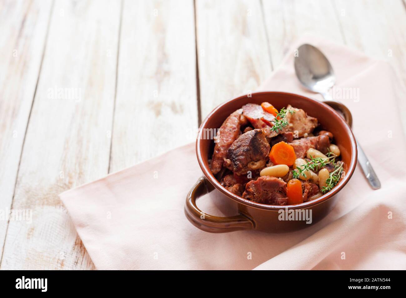 Cassoulet. Contenente salsicce di carne di maiale, oca, anatra e talvolta montone e due tipi di fagioli bianchi. Cibo francese. Su vecchio sfondo bianco di legno. Foto Stock