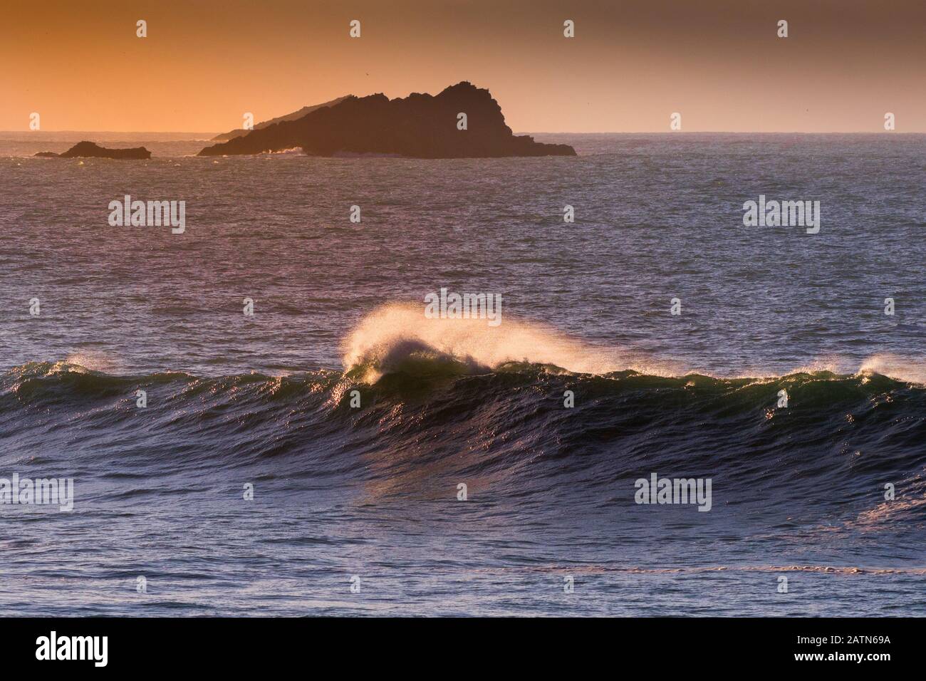 Un'onda che si infrangono in tarda serata con Goose Rock sullo sfondo della costa Newquay in Cornovaglia. Foto Stock