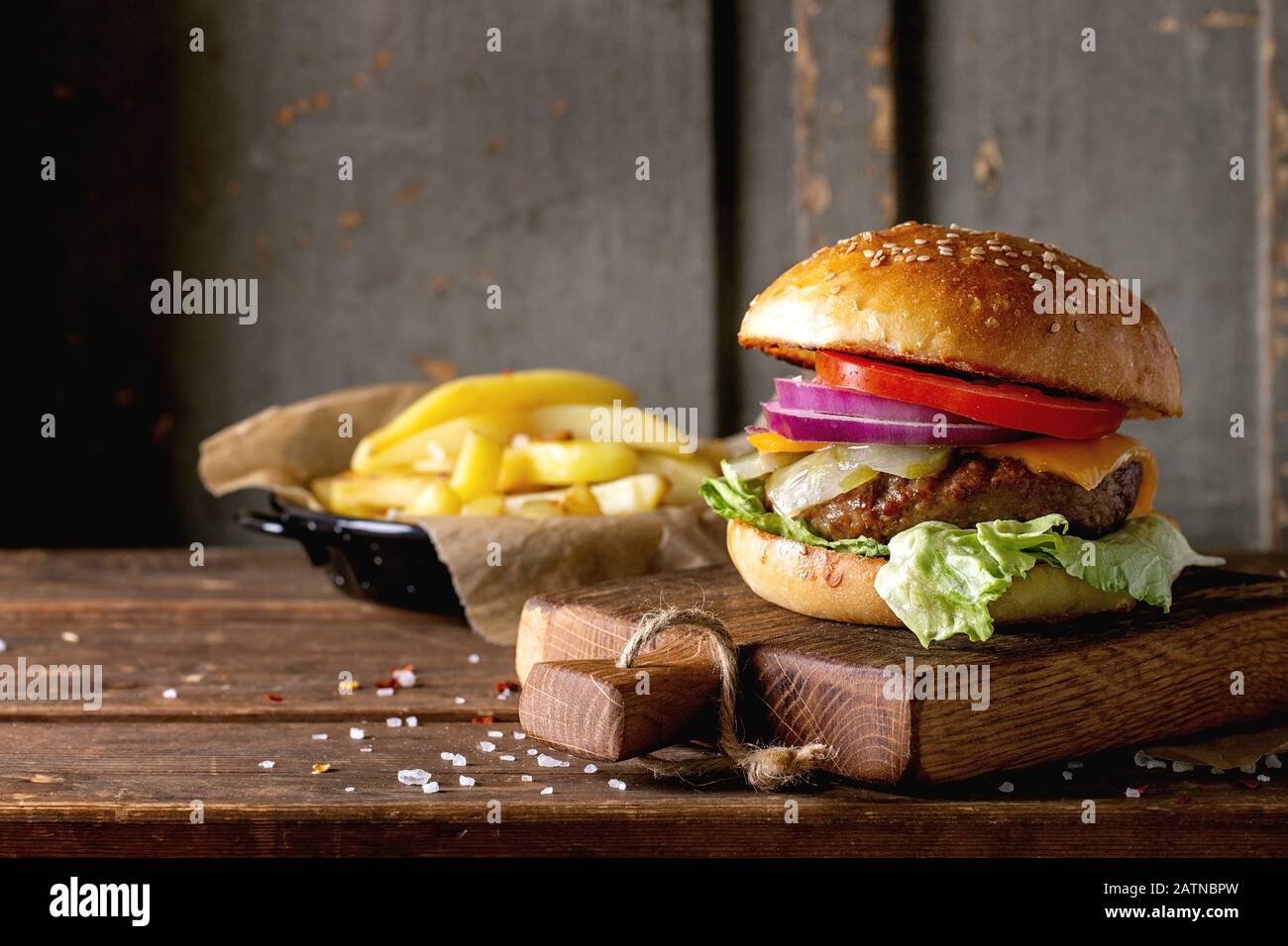 Freschi Fatti in casa burger sul piccolo tagliere con patate alla brace, servita con ketchup salsa e sale di mare su un tavolo di legno con grigio backgro in legno Foto Stock