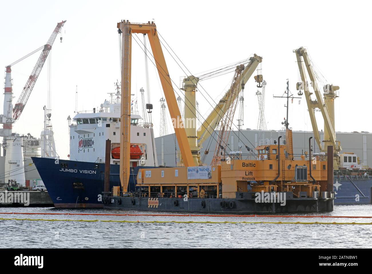 04 Febbraio 2020, Meclemburgo-Pomerania Occidentale, Rostock: Nel porto marittimo si trova la nave pesante "Jumbo Vision" che naviga sotto la bandiera olandese, da cui due gru portuali mobili sono cadute nel bacino del porto durante il loro carico in un incidente il 31.01.2020, di fronte al quale si trova la gru speciale "Baltic Lift" dei subacquei baltici. Le gru, che costano da tre a cinque milioni di euro, pesano ciascuna circa 440 tonnellate. Attualmente è in corso la lavorazione di un concetto di recupero, ma non è ancora stata fissata una data di sollevamento del calcestruzzo. Foto: Bernd Wüstneck/dpa-Zentralbild/dpa Foto Stock