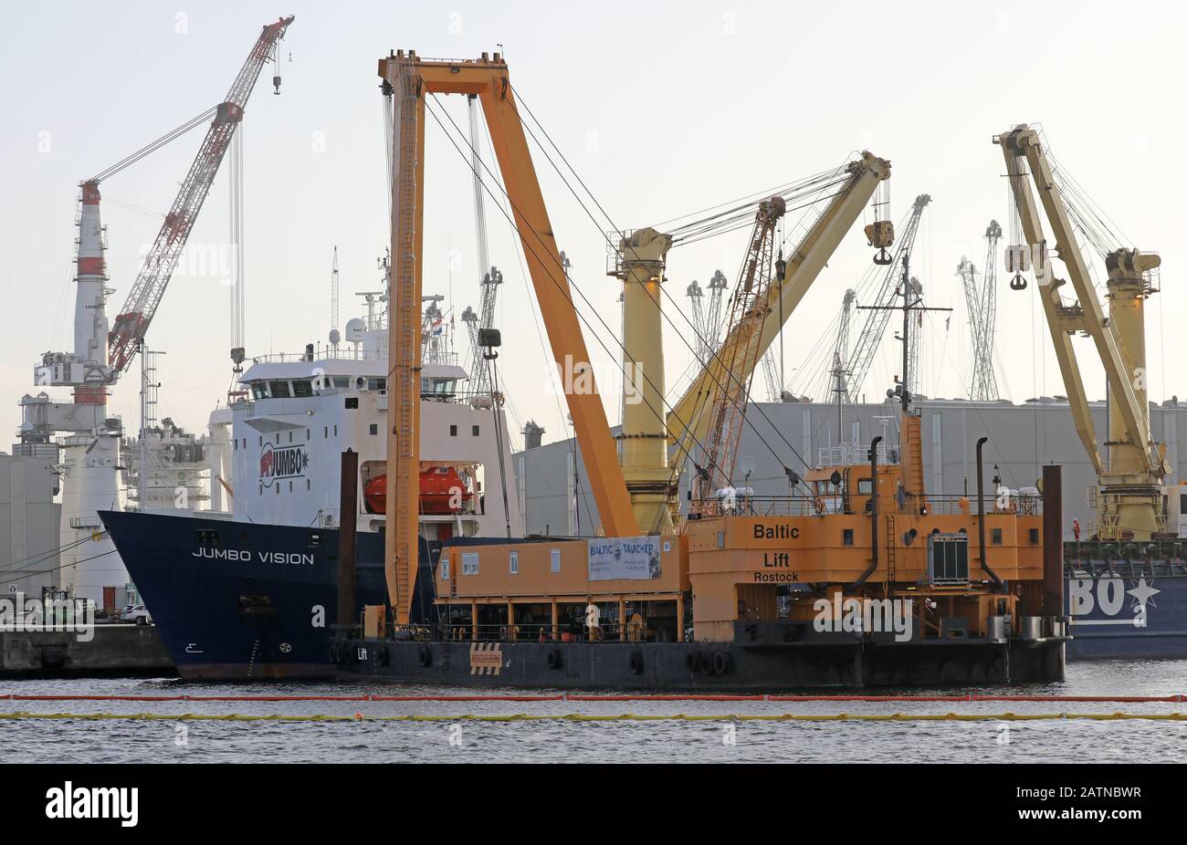 04 Febbraio 2020, Meclemburgo-Pomerania Occidentale, Rostock: Nel porto marittimo si trova la nave pesante "Jumbo Vision" che naviga sotto la bandiera olandese, da cui due gru portuali mobili sono cadute nel bacino del porto durante il loro carico in un incidente il 31.01.2020, di fronte al quale si trova la gru speciale "Baltic Lift" dei subacquei baltici. Le gru, che costano da tre a cinque milioni di euro, pesano ciascuna circa 440 tonnellate. Attualmente è in corso la lavorazione di un concetto di recupero, ma non è ancora stata fissata una data di sollevamento del calcestruzzo. Foto: Bernd Wüstneck/dpa-Zentralbild/dpa Foto Stock