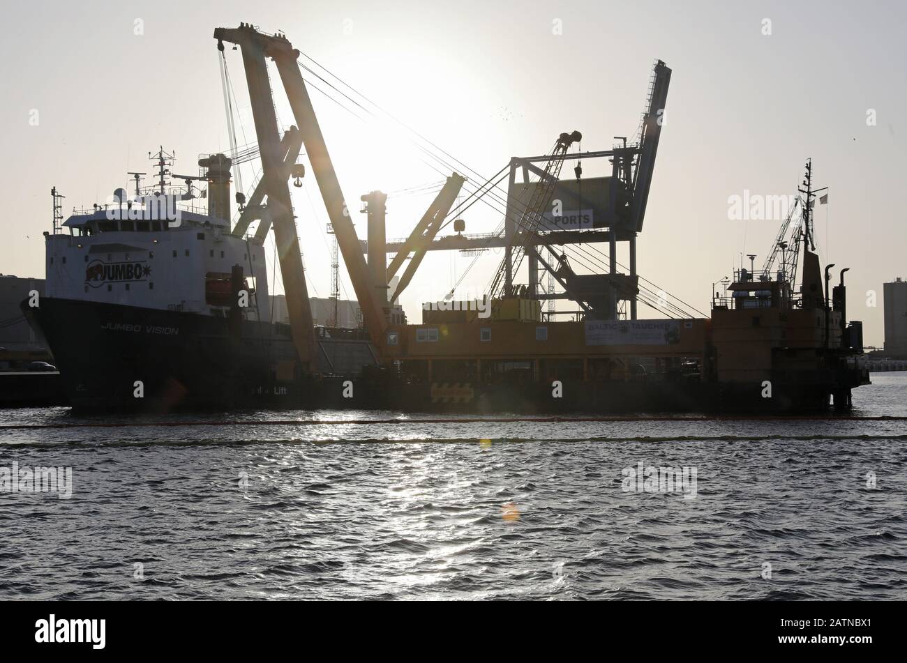 04 Febbraio 2020, Meclemburgo-Pomerania Occidentale, Rostock: Nel porto marittimo si trova la nave pesante "Jumbo Vision" (l) che naviga sotto la bandiera olandese, da cui due gru portuali mobili sono cadute nel bacino del porto durante il loro carico in un incidente il 31.01.2020, accanto ad esso (r) si trova la gru speciale "Baltic Lift" dei subacquei baltici. Le gru, che costano da tre a cinque milioni di euro, pesano ciascuna circa 440 tonnellate. Attualmente è in corso la lavorazione di un concetto di recupero, ma non è ancora stata fissata una data di sollevamento del calcestruzzo. Foto: Bernd Wüstneck/dpa-Zentralbild/dpa Foto Stock