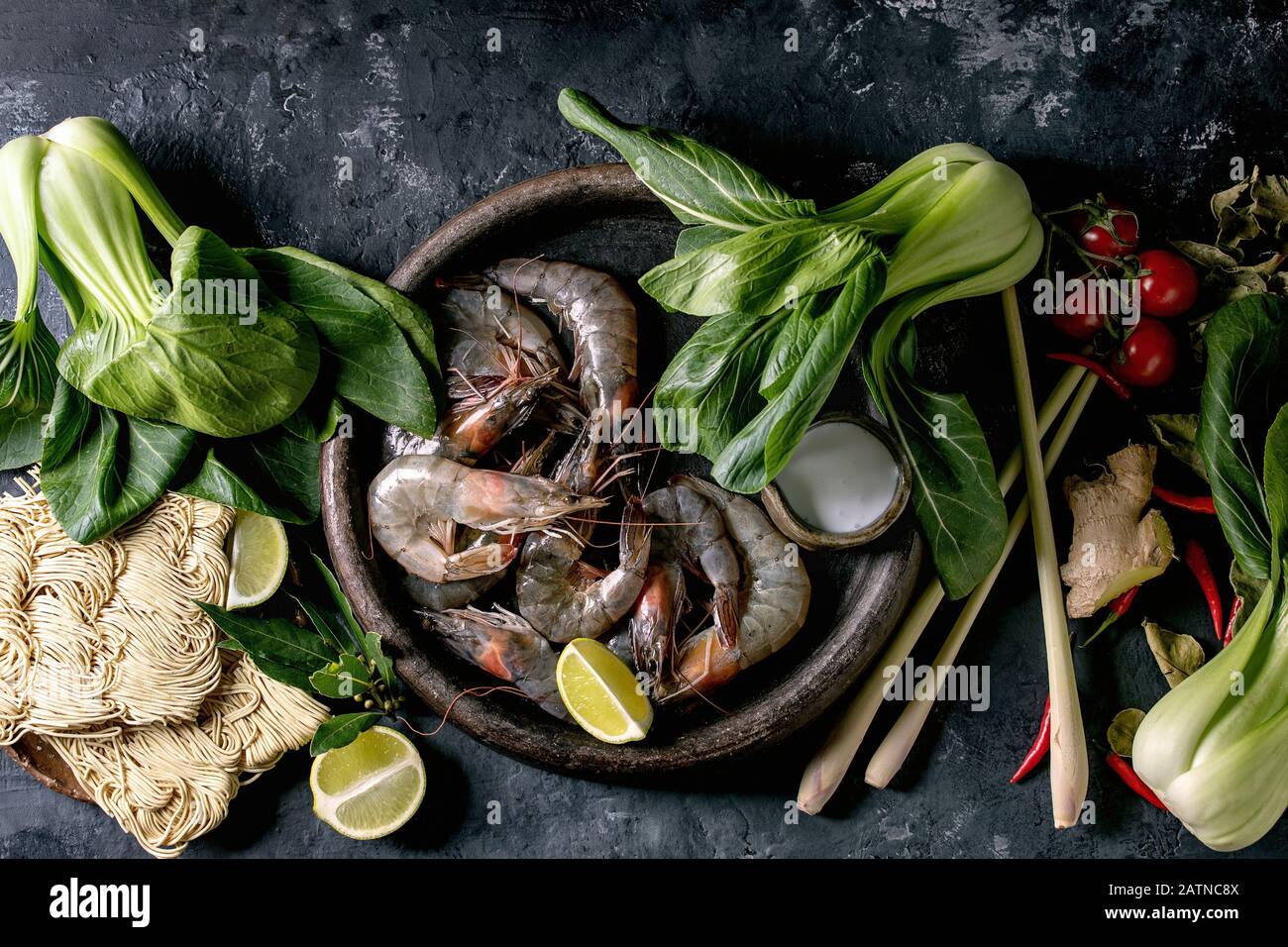 Gamberetti crudi con noodle asiatici, latte di cocnut e verdure. Ingredienti per cucinare una cena asiatica o una zuppa tailandese tom yum. Fondo in cemento scuro. Foto Stock