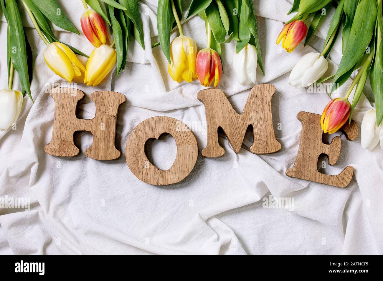 Lettere decorative in legno parola HOME con tulipani colorati su tessuto di cotone piegato. Disposizione piatta, spazio. Decorazione di casa di primavera. Foto Stock