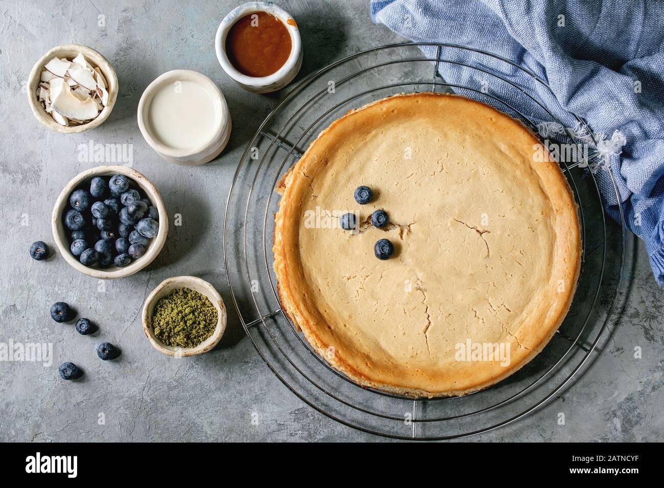 Cheesecake fatto in casa con zucchero di canna cotto su griglia di raffreddamento con varietà di condimenti in ciotole di ceramica su sfondo grigio texture. Disposizione piatta, spazio Foto Stock