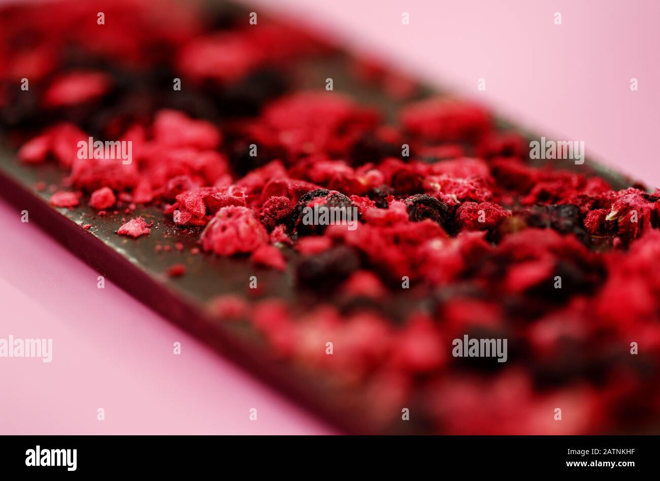Dark a basso contenuto calorico il cioccolato con secchi di bacche rosse sul rosa chiaro sfondo, il fuoco selettivo Foto Stock
