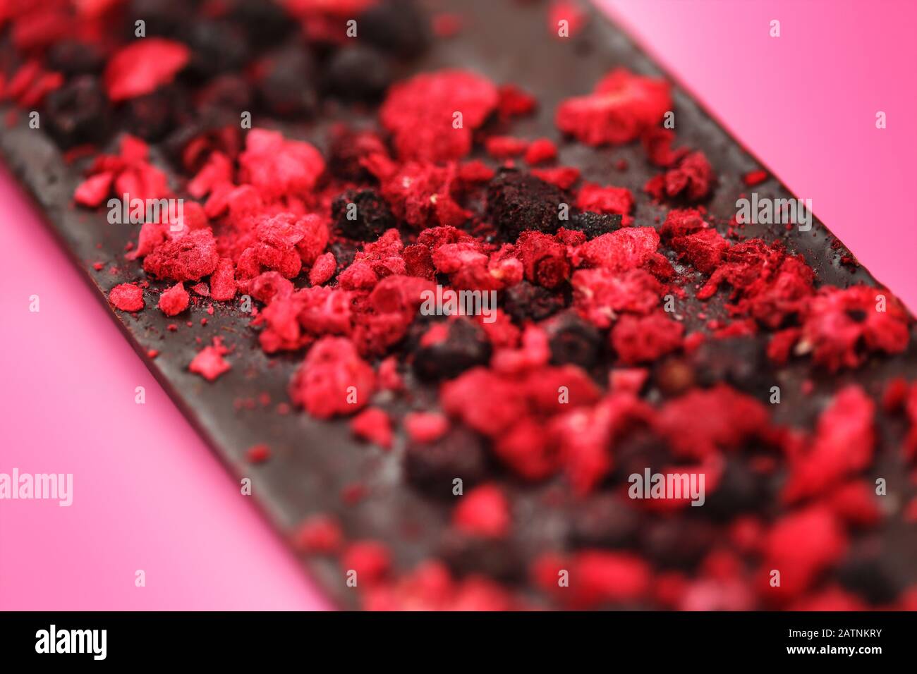 Dark a basso contenuto calorico il cioccolato con secchi di bacche rosse sul rosa chiaro sfondo, il fuoco selettivo Foto Stock