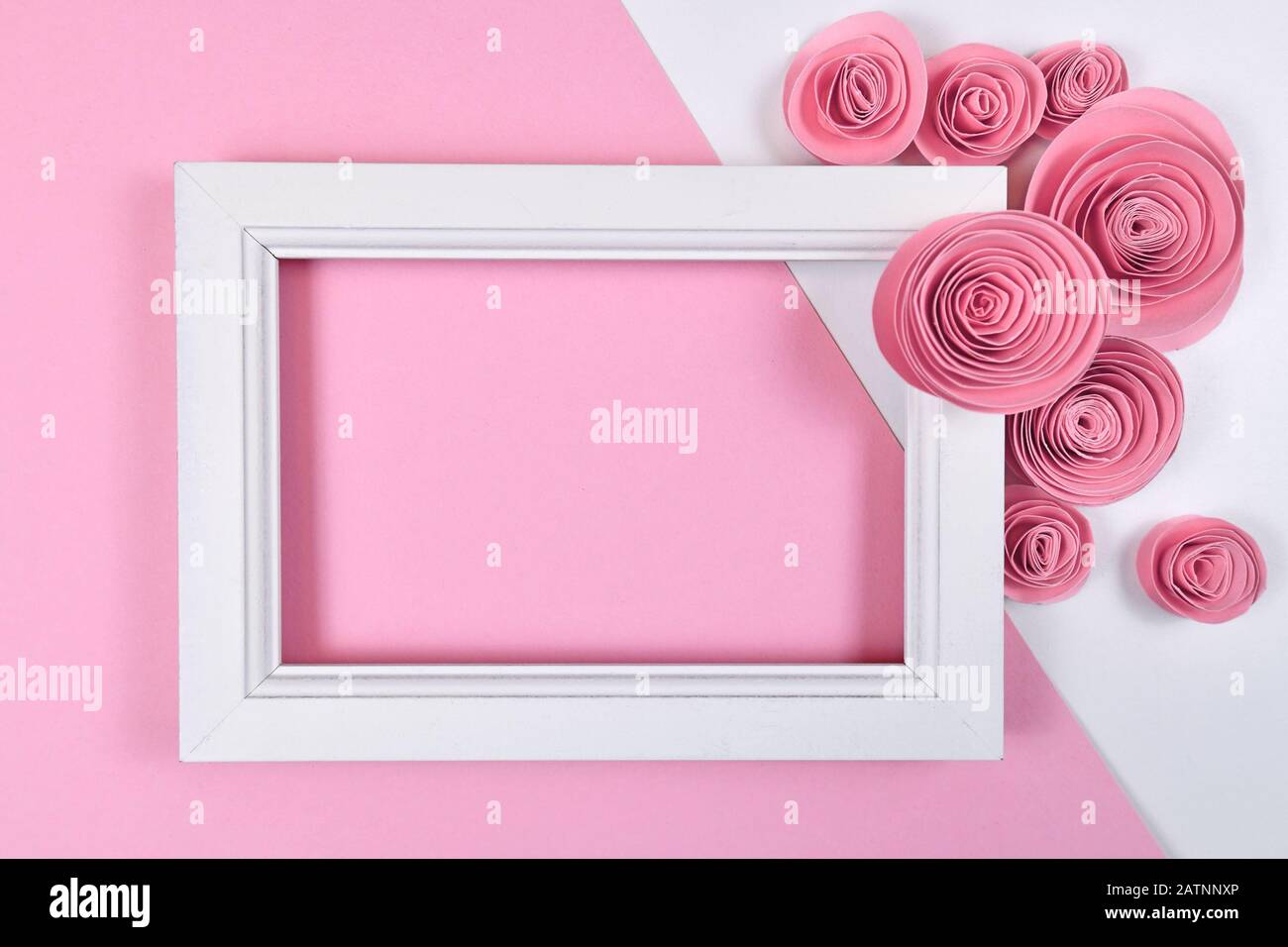 Romantica disposizione piatta con cornice bianca vuota circondata da rose artigianali di carta su sfondo rosa pastello Foto Stock