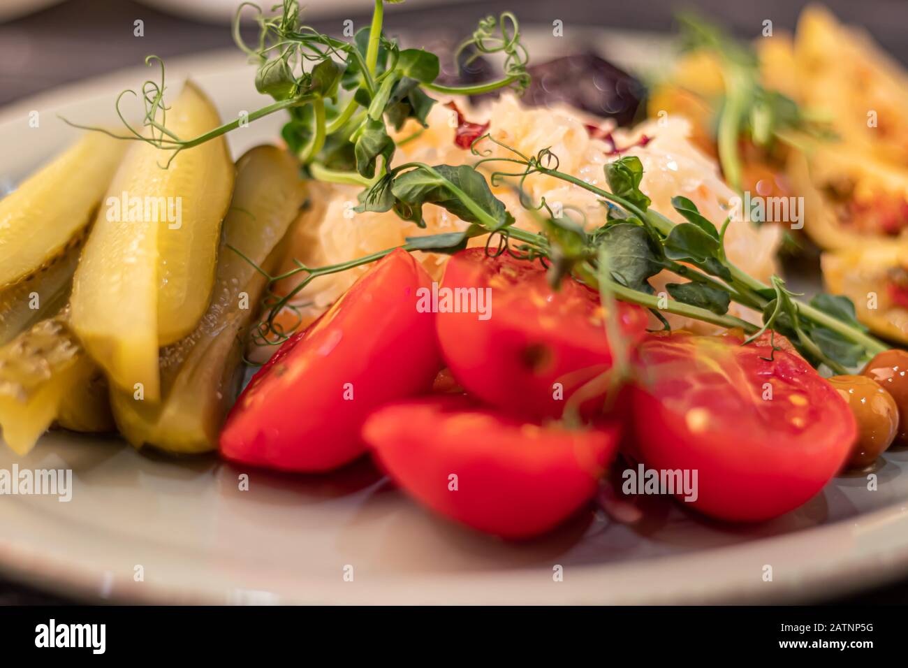 Verdure fermentate, salate ed erbe. Ingredienti per l'insalata. Cetrioli, pomodori, olive, crauti, prugne. A fette, decorato microgreen. Su un Foto Stock