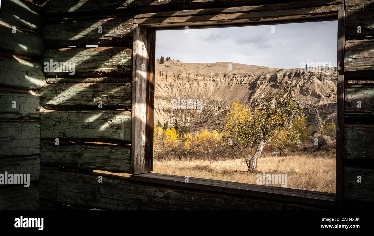 Guardando fuori la duna, hoodoos e alberi attraverso una finestra senza vetro di un edificio in legno deserto. (BC Canada) Foto Stock