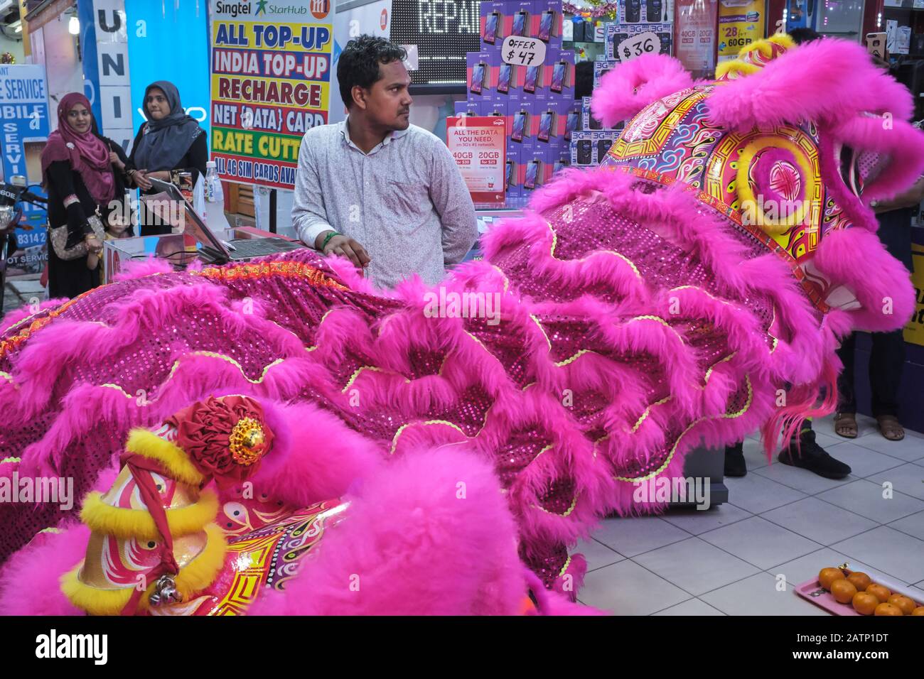 Una troupe cinese di danza del drago che esegue una danza del drago di fronte a un negozio nella zona Di Little India, Singapore, osservato da un assistente del negozio Foto Stock