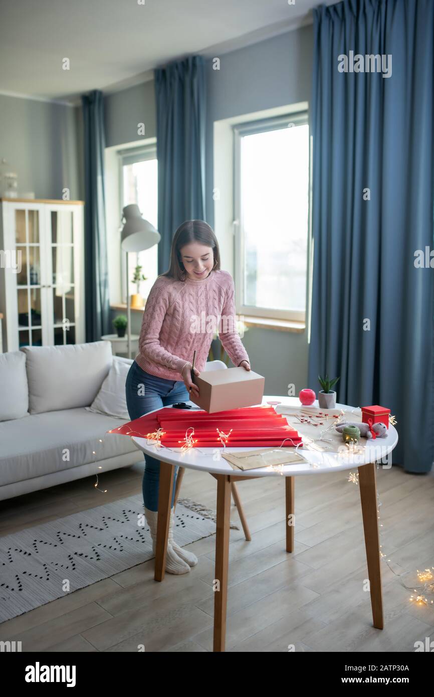 Ragazza dai capelli scuri in una camicia rosa che tiene una scatola attuale Foto Stock