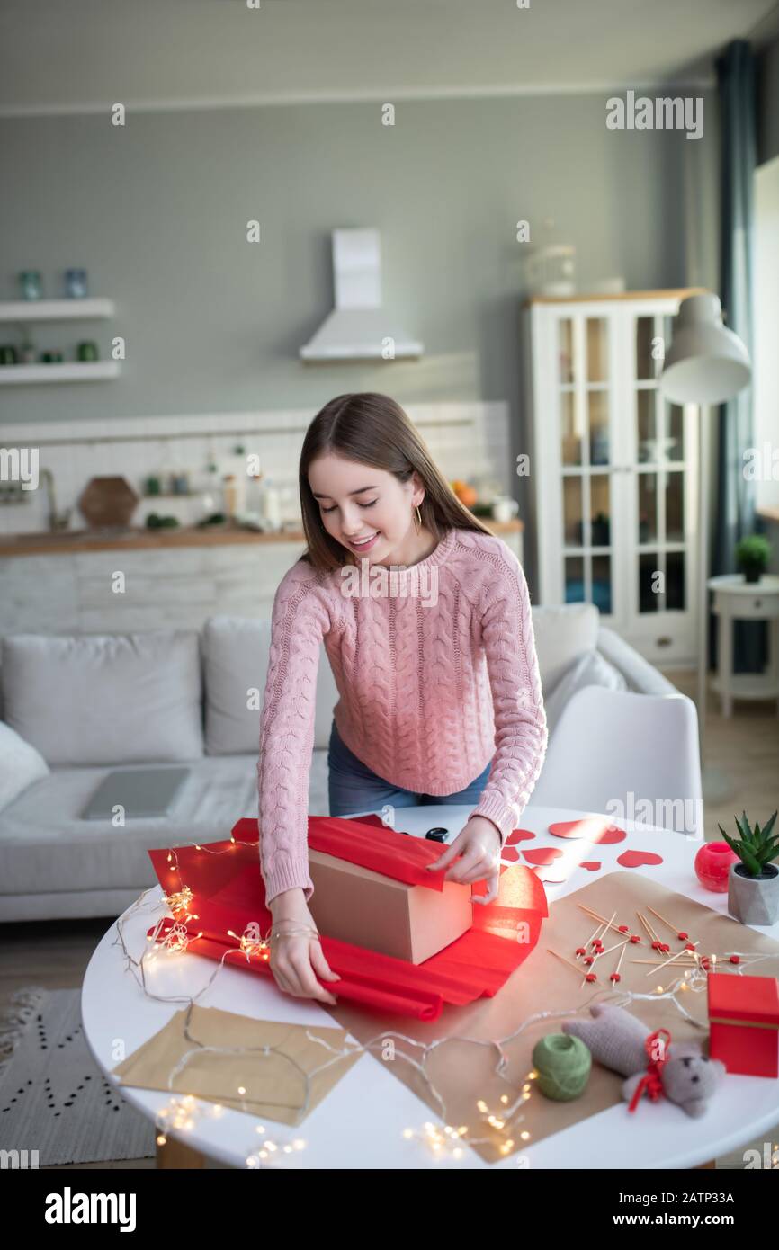 Capelli scuri con la ragazza di carta rossa in una camicia rosa che copre una scatola del regalo Foto Stock