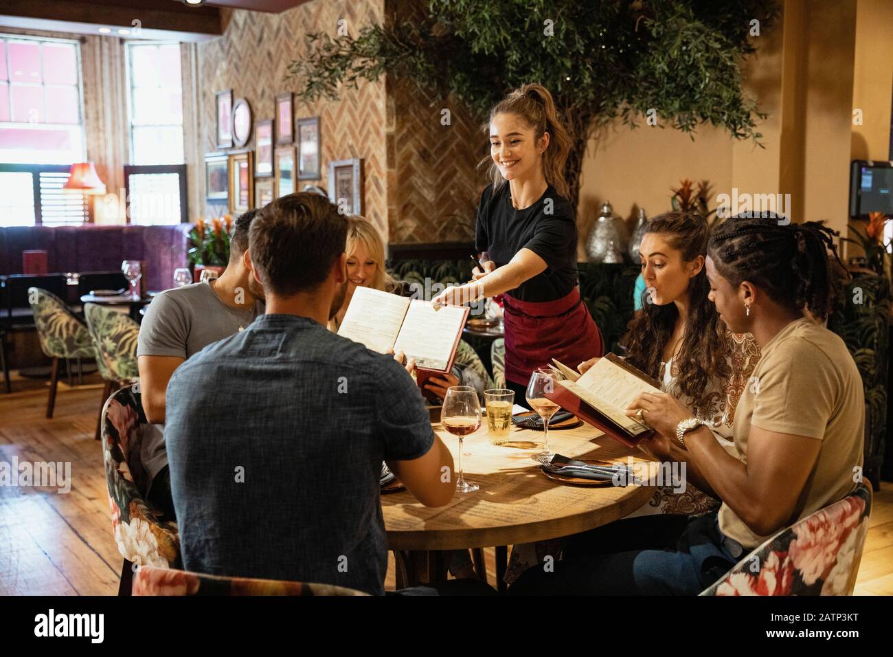 Un gruppo multietnico di amici che guardano i menu insieme in un ristorante, che sono stati loro dati da una cameriera. Foto Stock