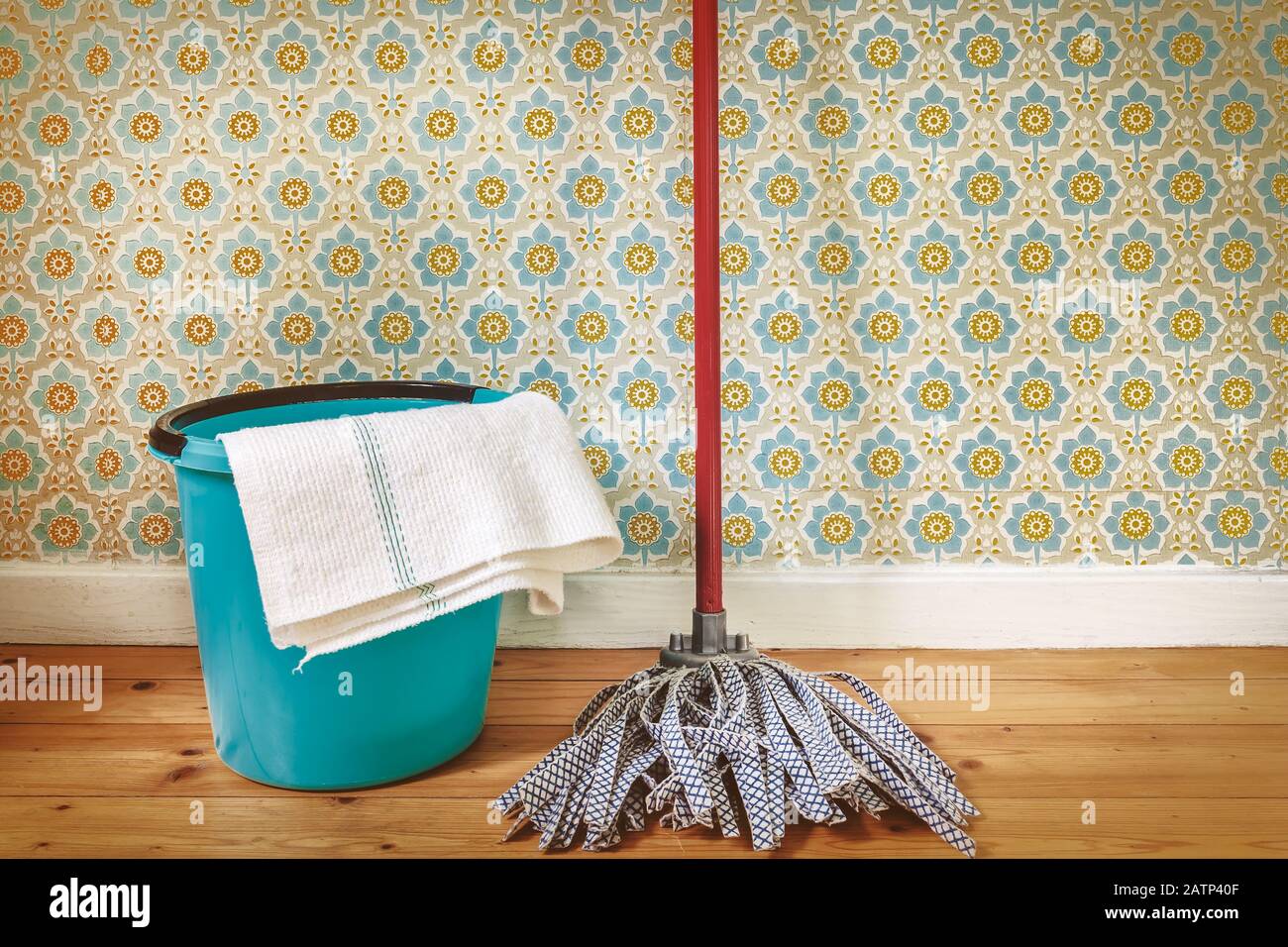 Immagine tonalità seppia di un mop e secchio sul pavimento di fronte alla carta da parati retrò Foto Stock