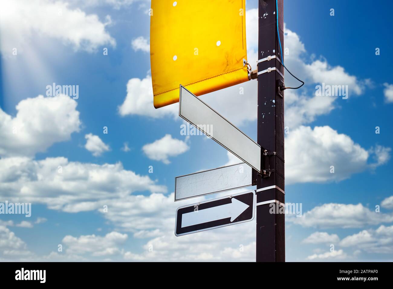Segnali stradali vuoti o segnali stradali e un banner sulla pole sullo sfondo blu nuvoloso del cielo. Simulazione del design con spazio di copia. Foto Stock